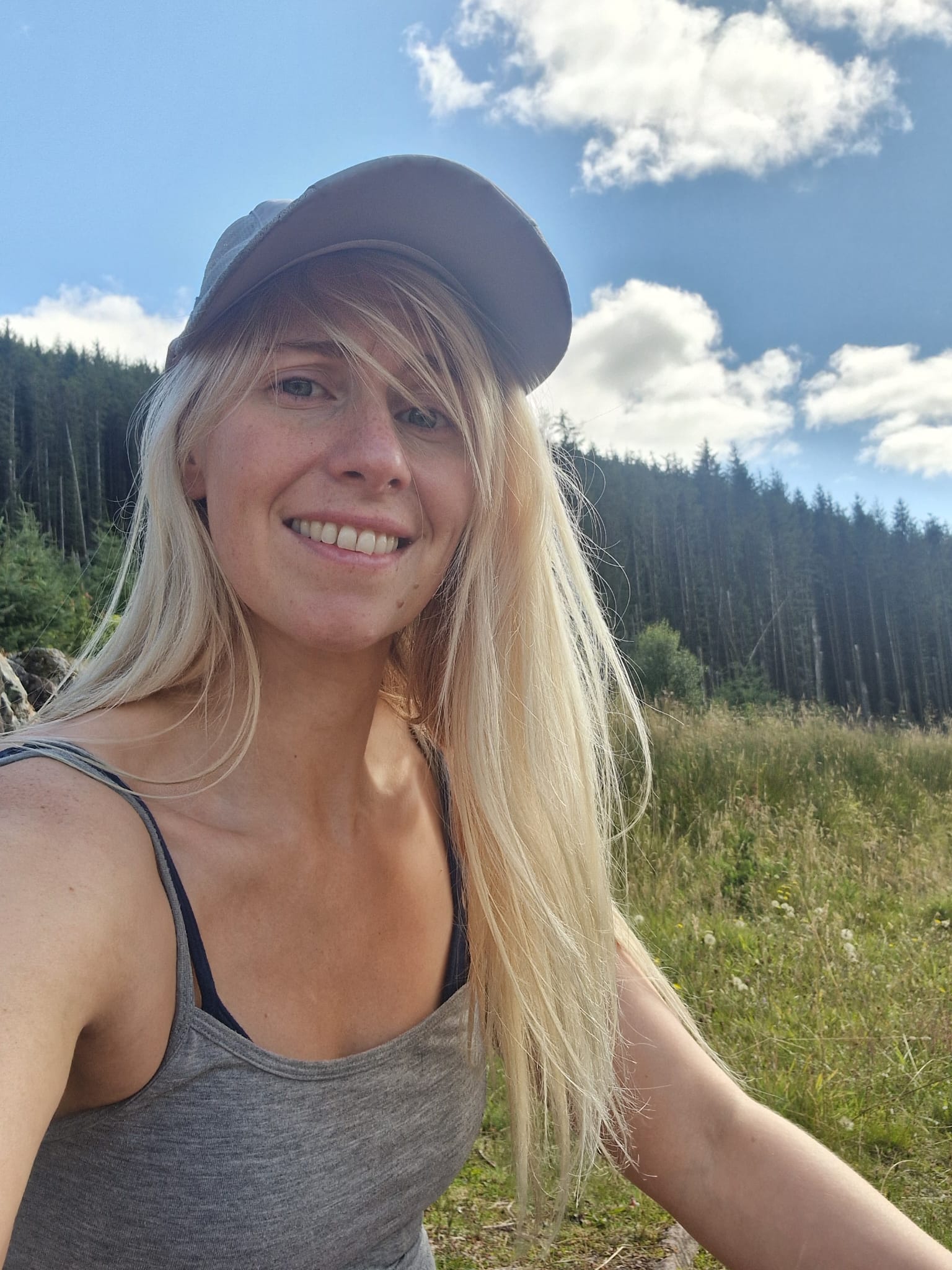 Danielle smiling outdoors with trees and blue sky behind her